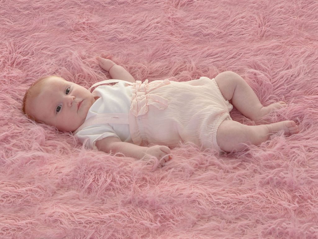 newborn baby girl lying on a pink fur rug