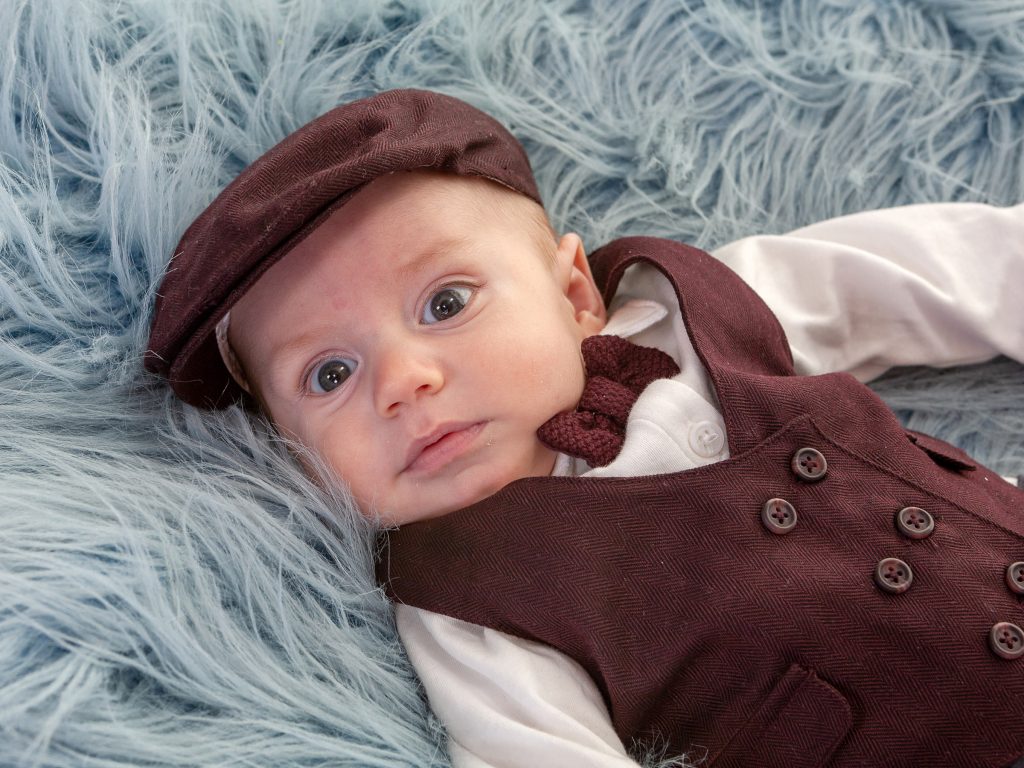 little newborn baby boy with flat cap staring into camera
