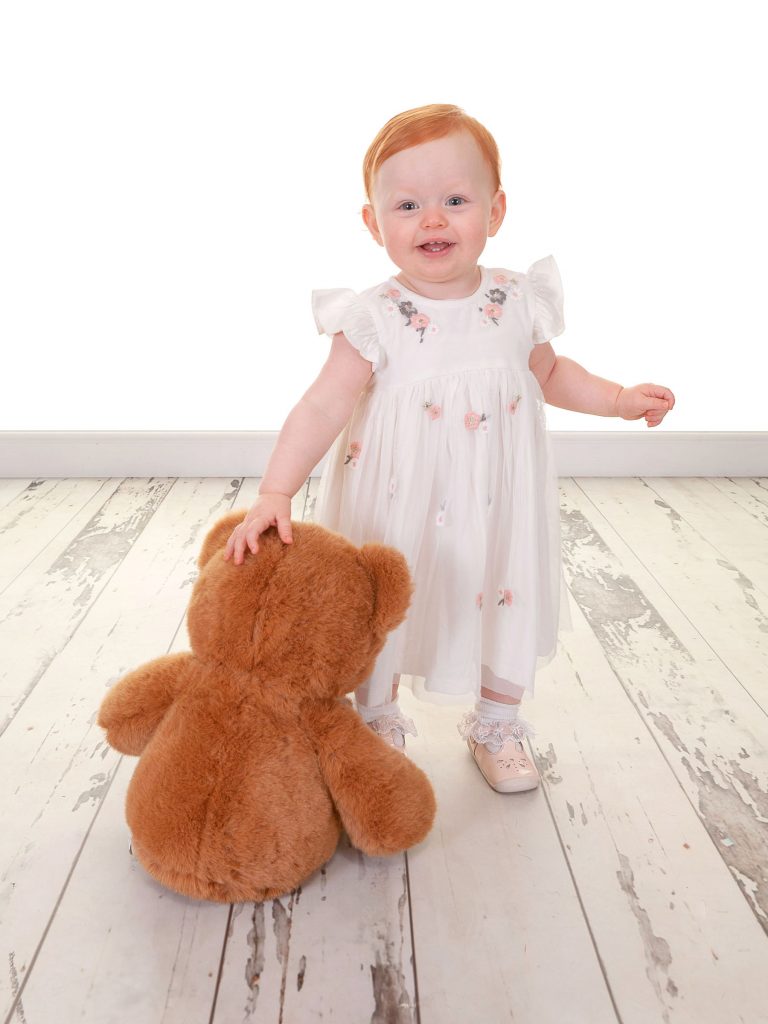 Little baby girl with ginger hair stood up holding her teddy bear
